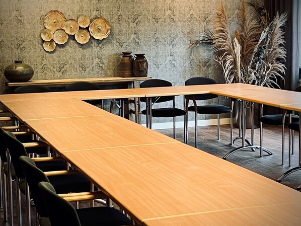 Una sala de conferencias con largas mesas de madera y sillas negras, una pared con textura y decoración mural.