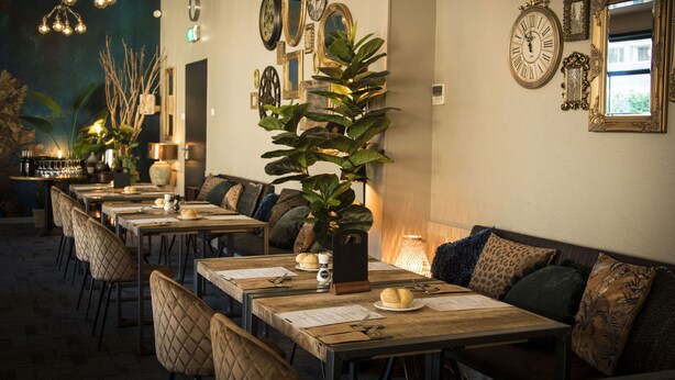 A restaurant with multiple tables and chairs, a large plant centerpiece, and various wall decorations including clocks and mirrors.