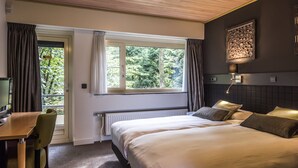 A bedroom with a large bed, a desk, and a window with curtains.