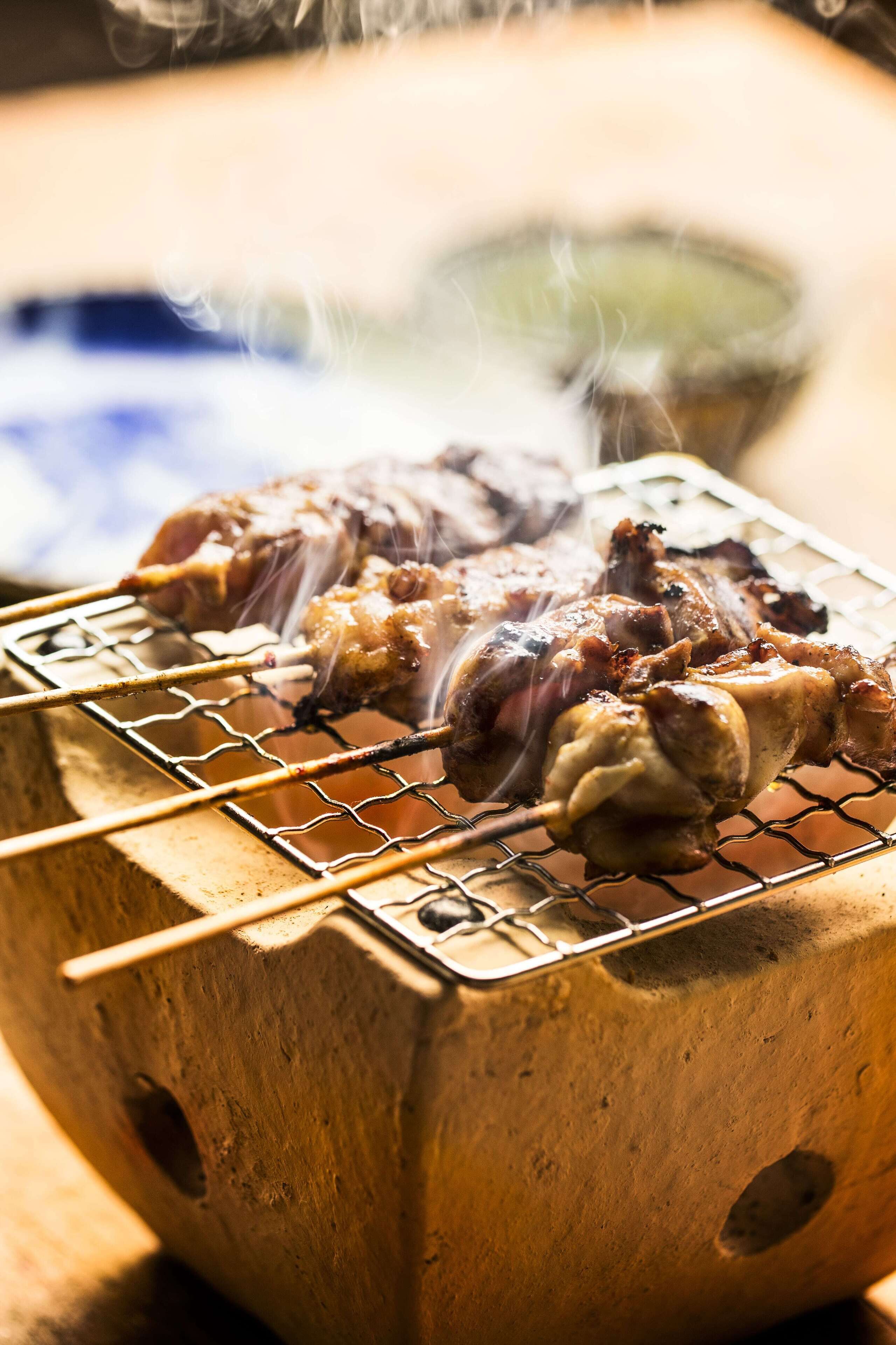 A grill with skewered meat, a wooden block, and a bowl in the background.