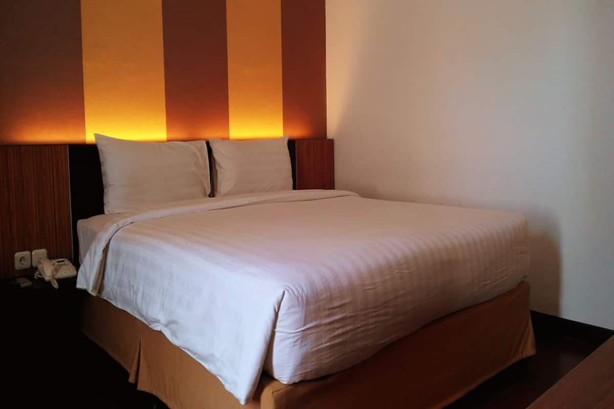 Una habitación de hotel con una cama grande, cabecera de madera y una pared con rayas verticales.
