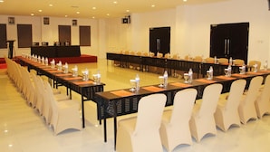 A conference room with long tables, chairs, and a stage. - Hotel Grand Imawan (Makassar)