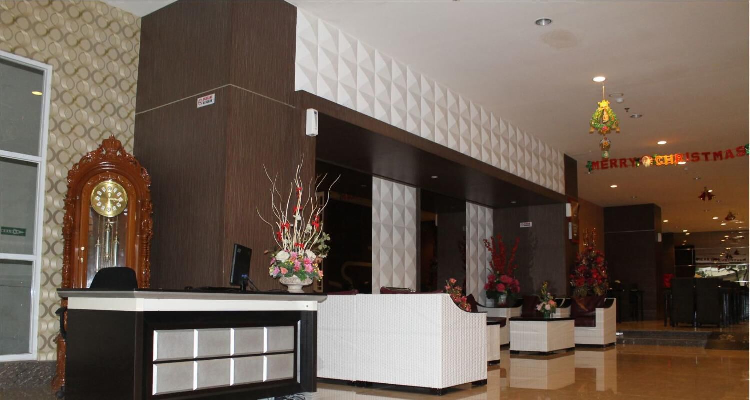 A hotel reception area with a wooden reception desk, a large wall clock, and a 'Merry Christmas' sign.