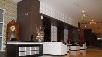 A hotel reception area with a wooden reception desk, a large wall clock, and a 'Merry Christmas' sign.