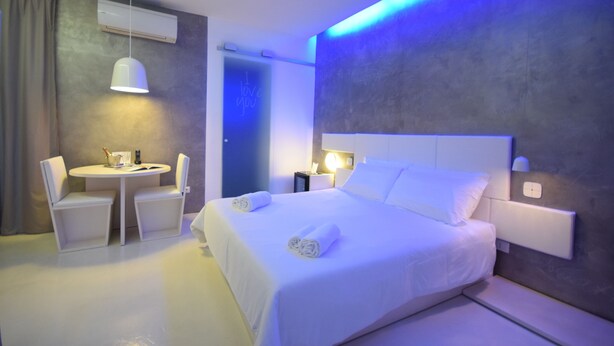 Una habitación de hotel moderna con una cama grande, una mesita de noche, una silla y una pequeña mesa con lámpara.