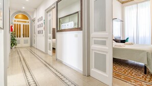 A hotel corridor with a patterned floor, a reception desk, a bed with a white bedspread, and a large mirror. - El Dorado Colosseum (Rome)