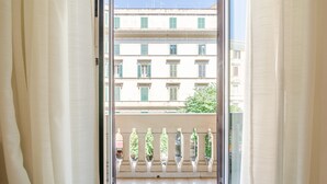 A view through a window with a balcony, featuring a building with multiple windows and a tree. - El Dorado Colosseum (Rome)