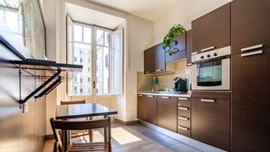 A modern kitchen with a dining area, featuring a large window, dark wooden cabinets, and a built-in oven. - El Dorado Colosseum (Rome)