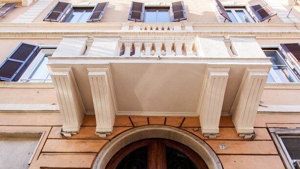 A building facade with a large wooden double door, a balcony with sun louters, and a number '73' sign. - El Dorado Colosseum (Rome)
