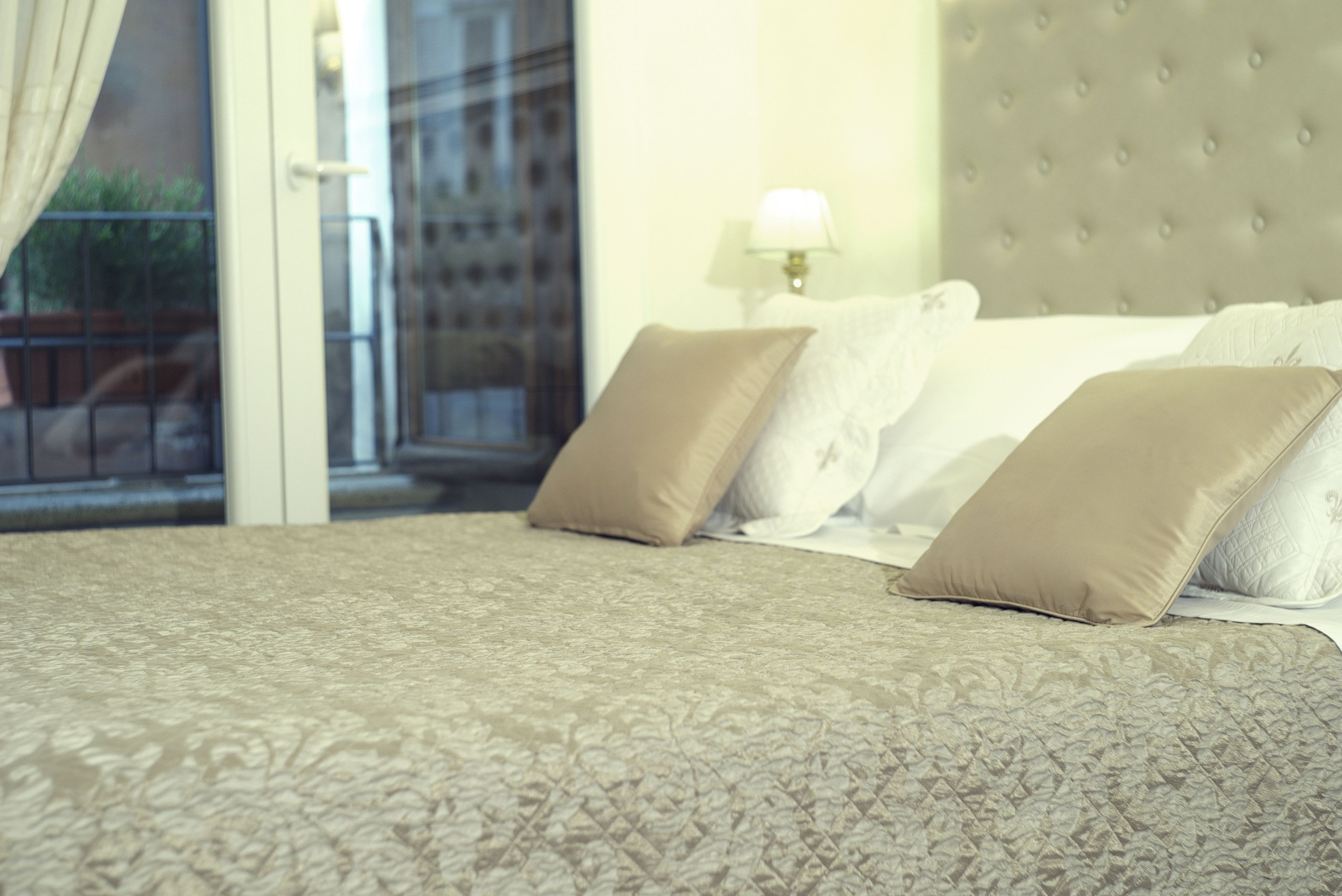 A hotel room with a bed, pillows, a lamp, and a view through a window.