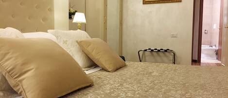 A hotel room with a large bed, a headboard, a bedside table with a lamp, a mirror, and a framed picture on the wall.