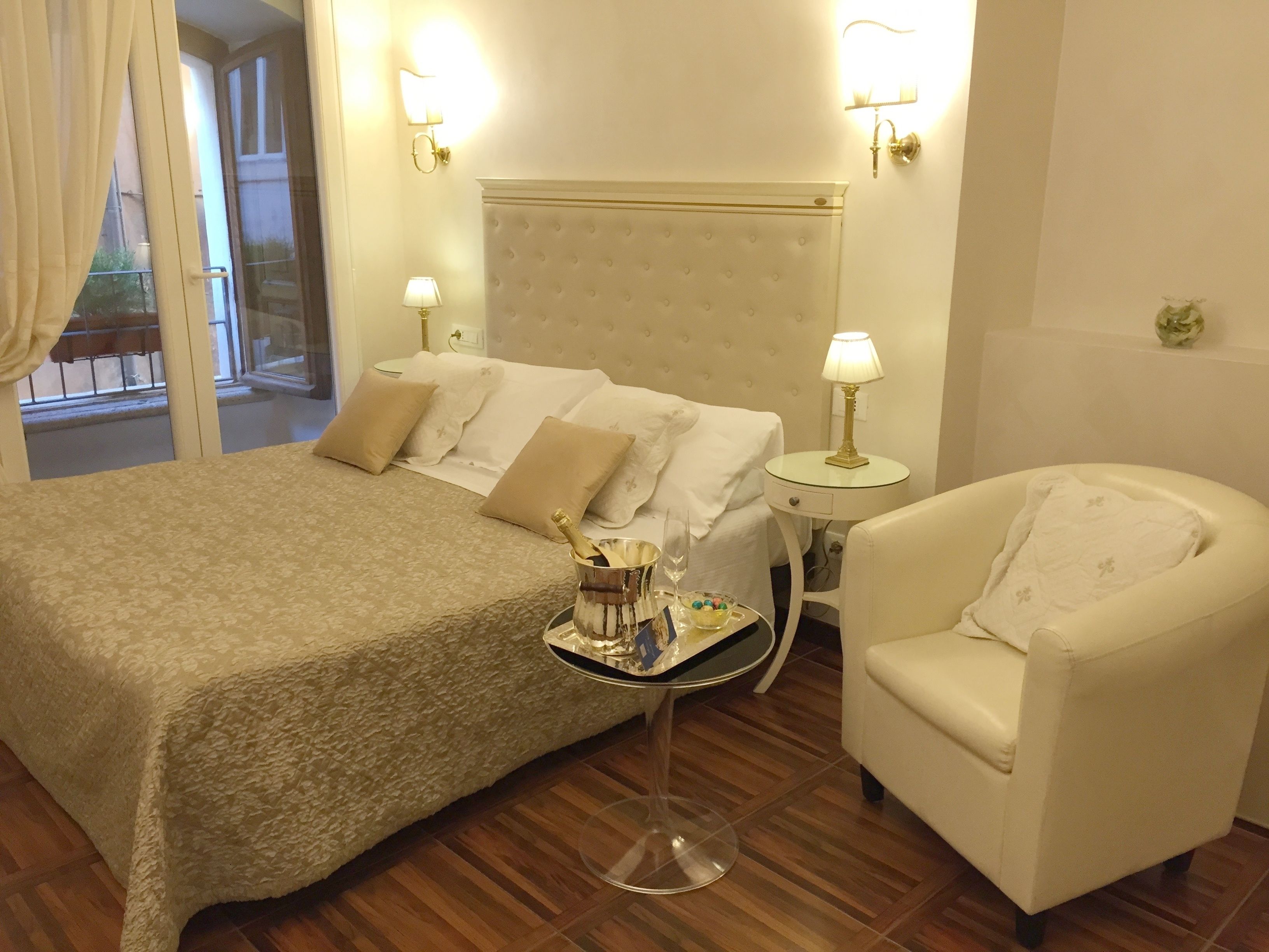 A hotel room with a bed, a chair, a bedside table with a lamp, and a view of the outside.