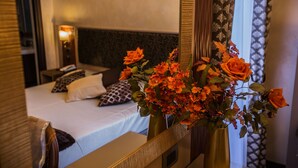 A hotel room with a bed, pillows, a bedside table, and a mirror reflecting a vase with orange flowers. - Hotel Romano (Rome)
