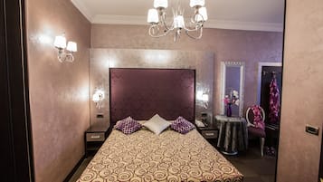A hotel room with a large bed, a chandelier, a vanity with a mirror, and a robe hanging on a hook.