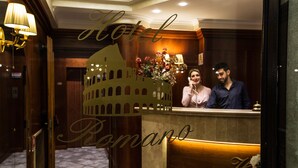A hotel reception area with a large, illuminated colosseum cutout, a reception desk, and a floor with a patterned tile design. - Hotel Romano (Rome)
