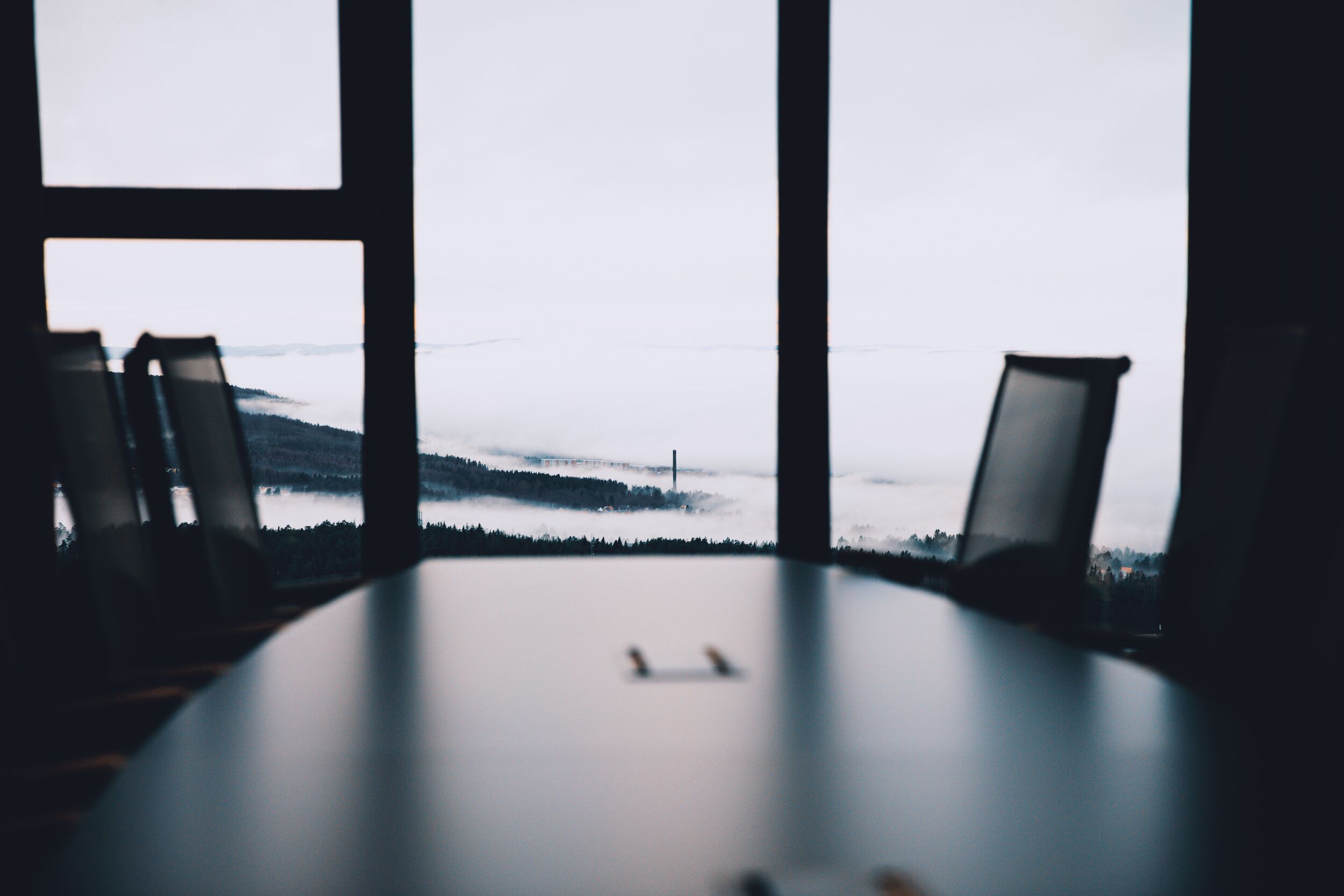 Une salle de conférence équipée d’une table et de quatre chaises, donnant sur un paysage brumeux grâce à de grandes fenêtres.