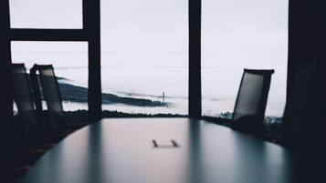 Un salón de conferencias con una mesa y cuatro sillas, con vistas a un paisaje brumoso a través de amplias ventanas.