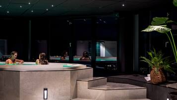 A modern spa area with a reception desk, a seating area, and a large window providing a view of the cityscape at night.
