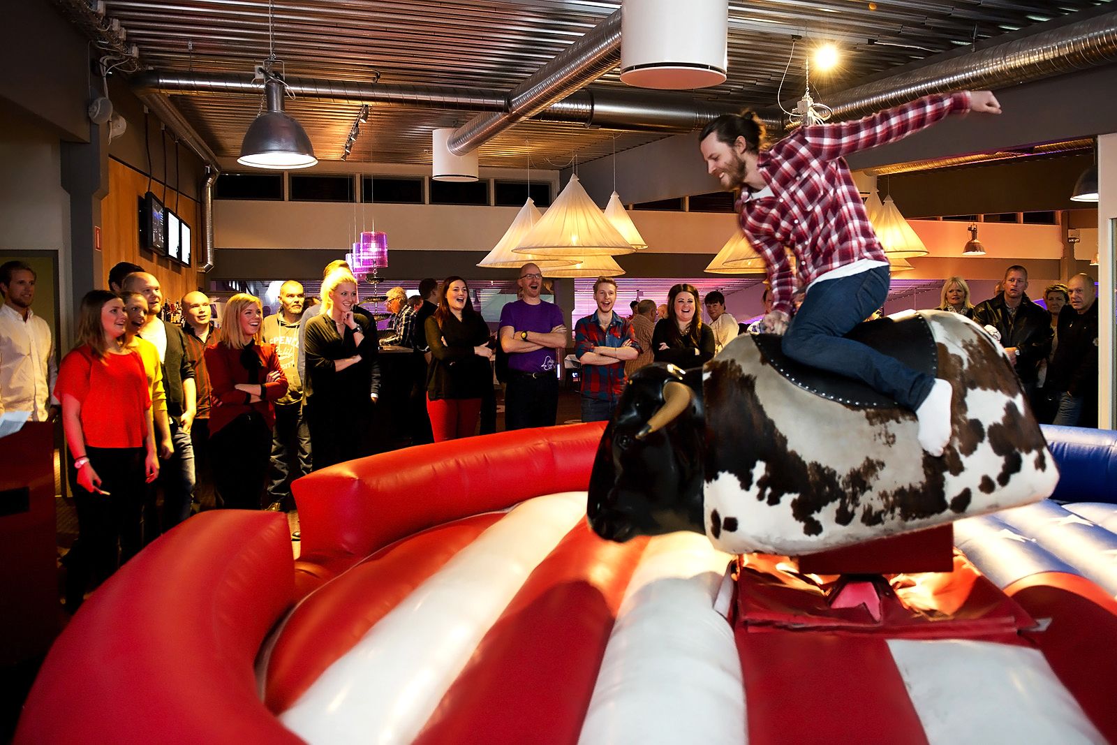 A person riding an inflatable bull in a room with a crowd watching.