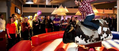 A person riding an inflatable bull in a room with a crowd watching.