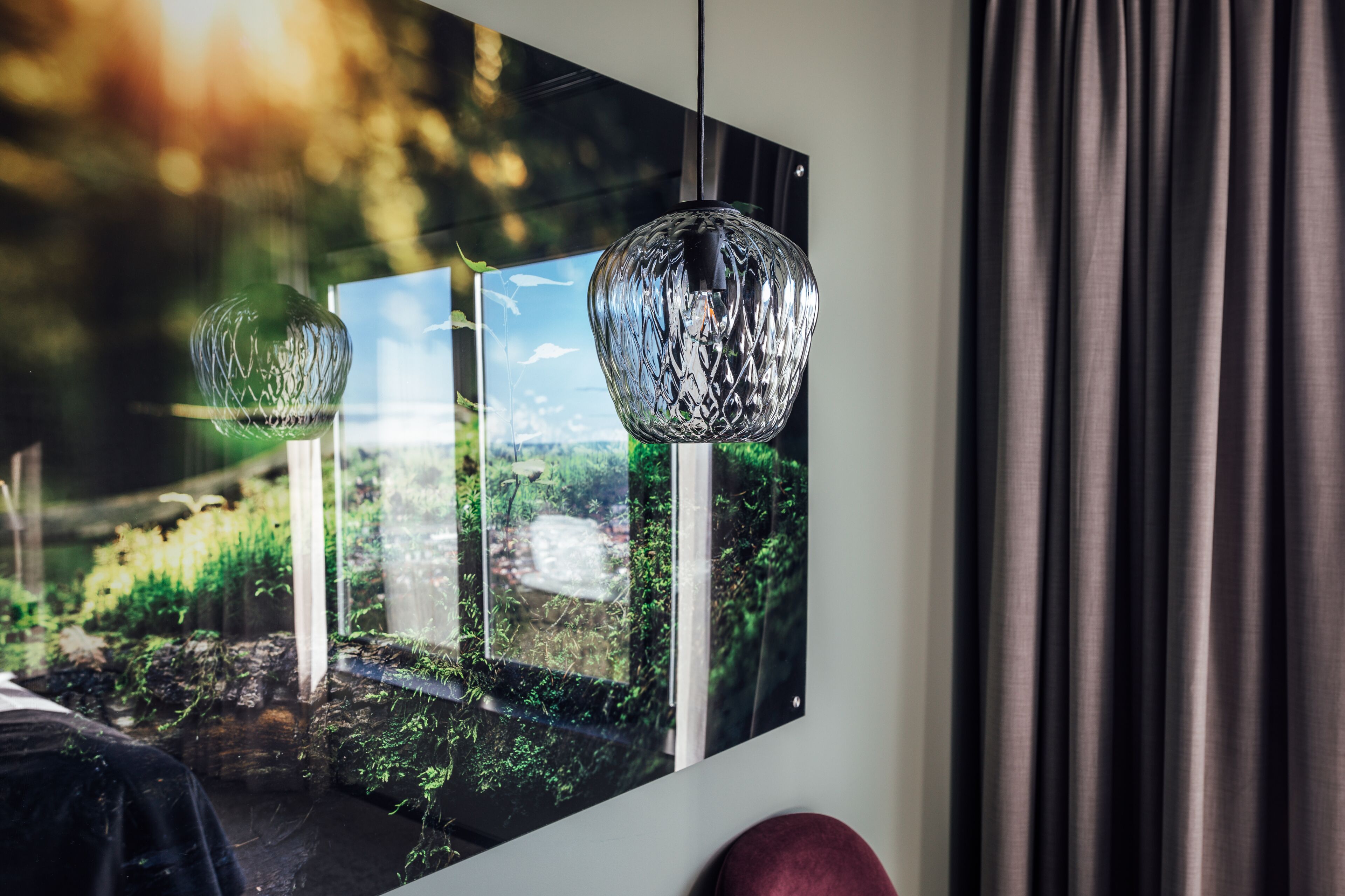 Quarto com uma grande moldura com uma paisagem, duas luminárias de cristal penduradas e vista para um jardim pela janela.
