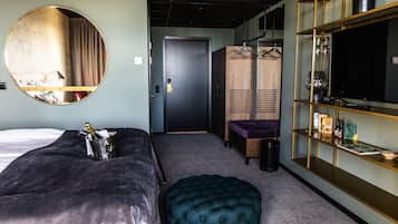 Una habitación de hotel con cama, espejo redondo, armario, zona de estar y televisor en un estante.