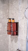 Un baño con pared de mármol y estante con dos botellas de jabón para manos.