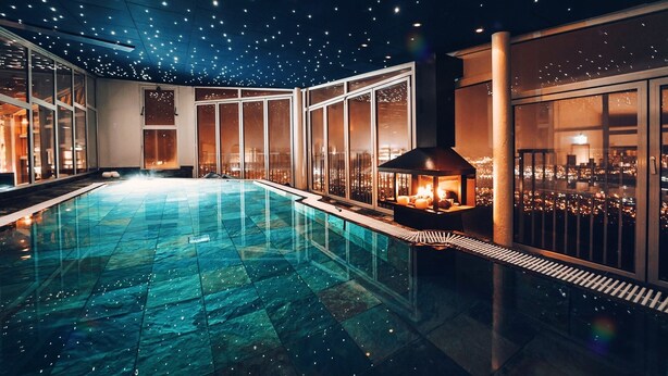 Una piscina interior moderna con techo estrellado, ventanas amplias y chimenea.