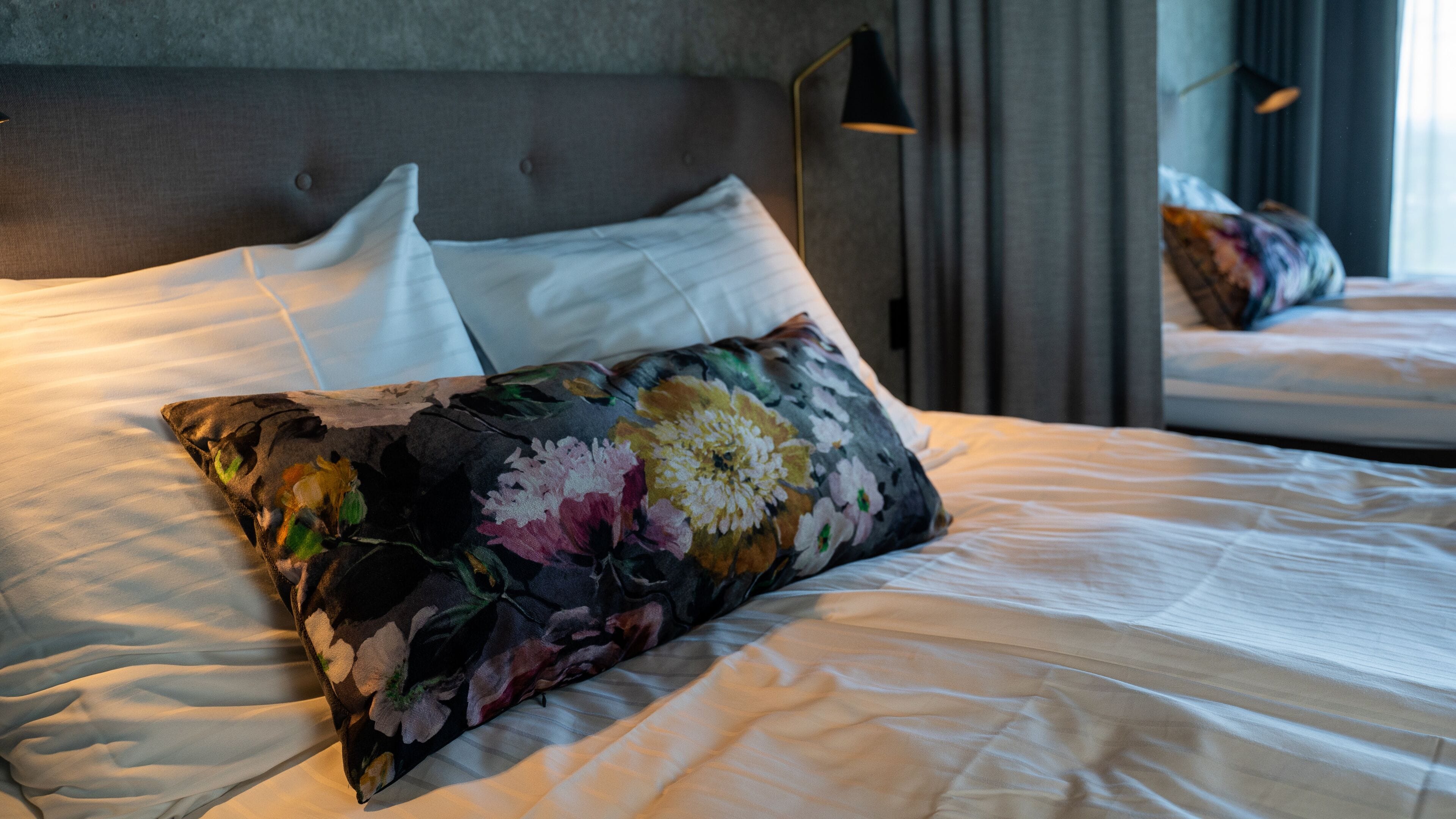 Una cama bien hecha con sábanas blancas y una almohada estampada.