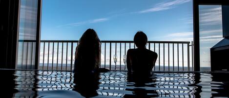 A couple sitting by a pool with a view of the sea.