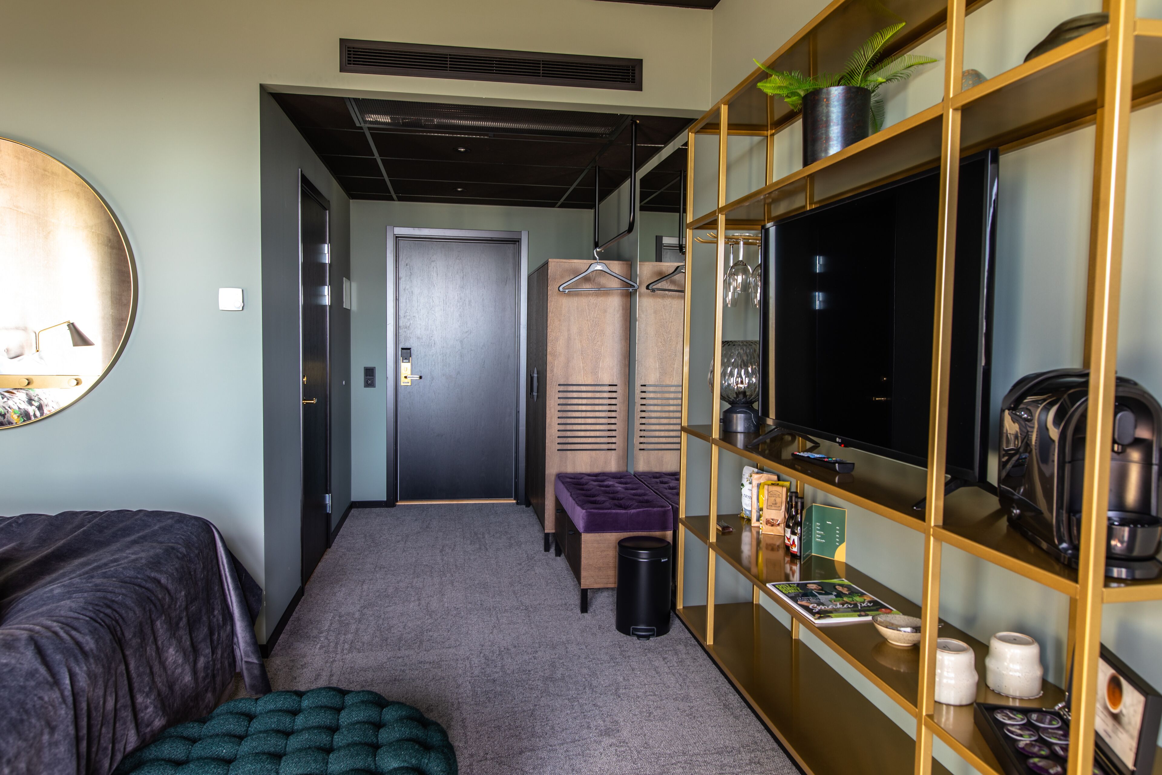 A hotel room with a bed, a seating area, a TV, a bookshelf, and a trash bin.