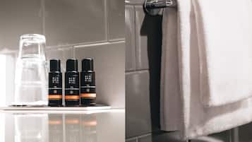 A bathroom with a white towel hanging on a rack, a glass bottle, and three black bottles labeled 'Rituals' with different contents.