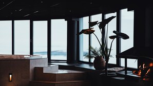 Un interior moderno con chimenea, ventanas amplias y vista al mar.