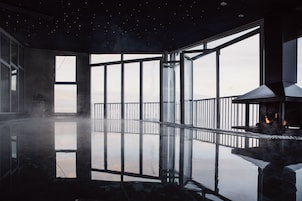 Una habitación amplia con ventanas grandes, piso reflectante y una chimenea moderna.