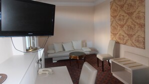Ett modernt hotellrum med en platt-TV, en soffa, ett soffbord och ett litet sidobord.