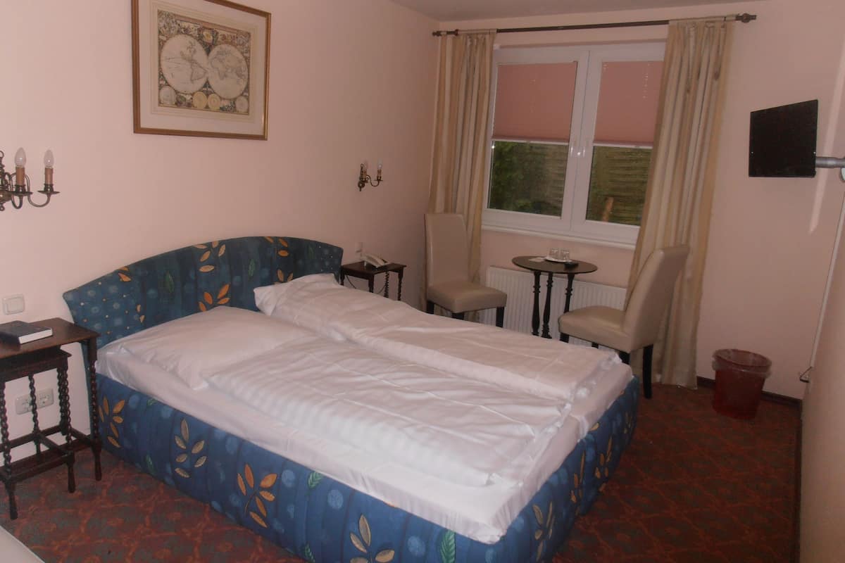 A double bed with a floral headboard, a small bedside table, a chair, a window with curtains, and a wall-mounted globe.
