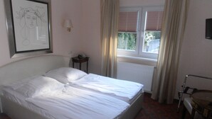 Ett hotellrum med en säng, ett nattduksbord med en lampa, ett fönster med gardiner och en inramad tavla på väggen.