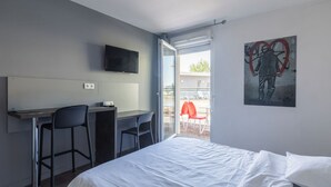 A hotel room with a bed, a desk with chairs, a television, and a painting on the wall.