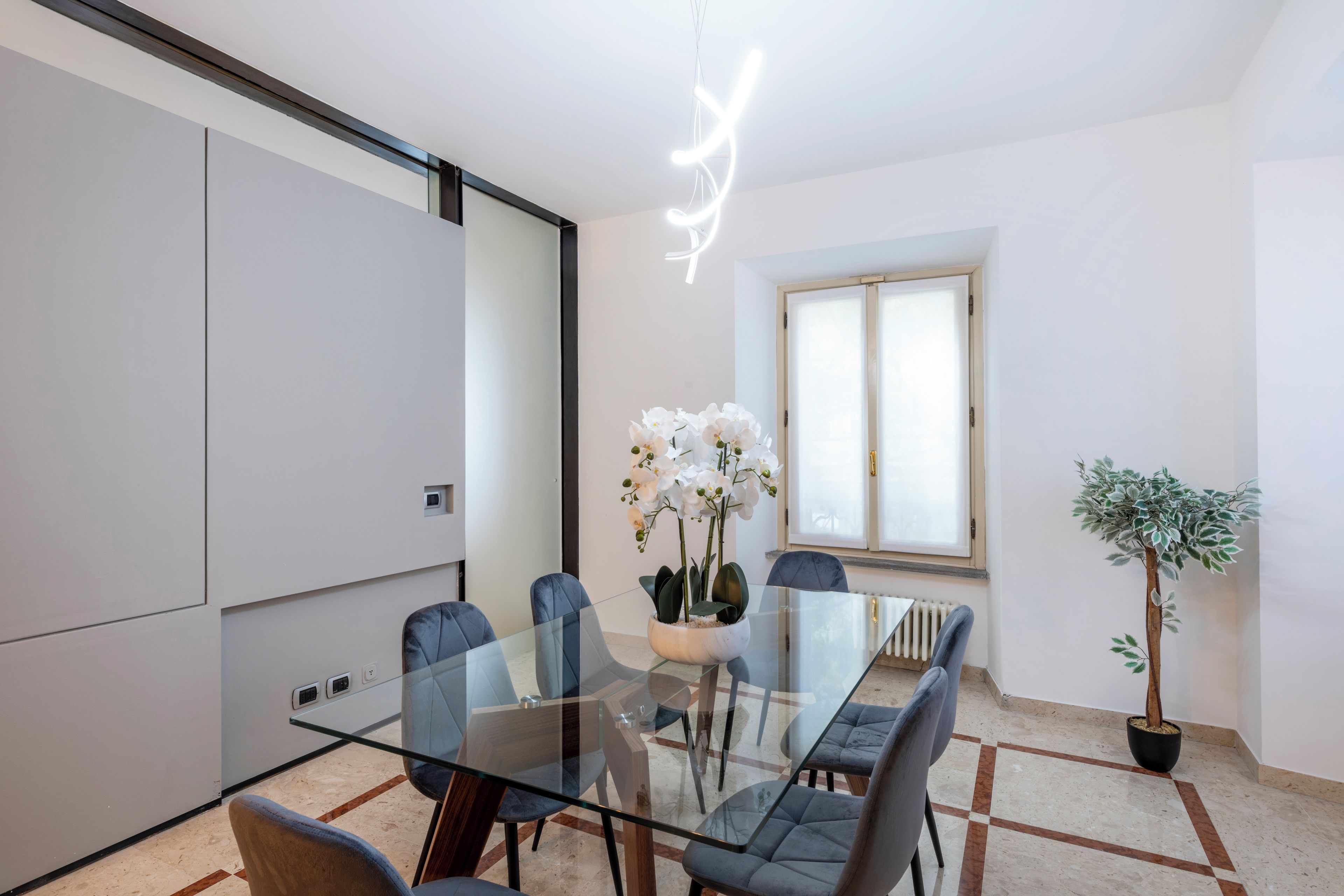 A modern dining area with a glass table, blue chairs, and a potted plant.