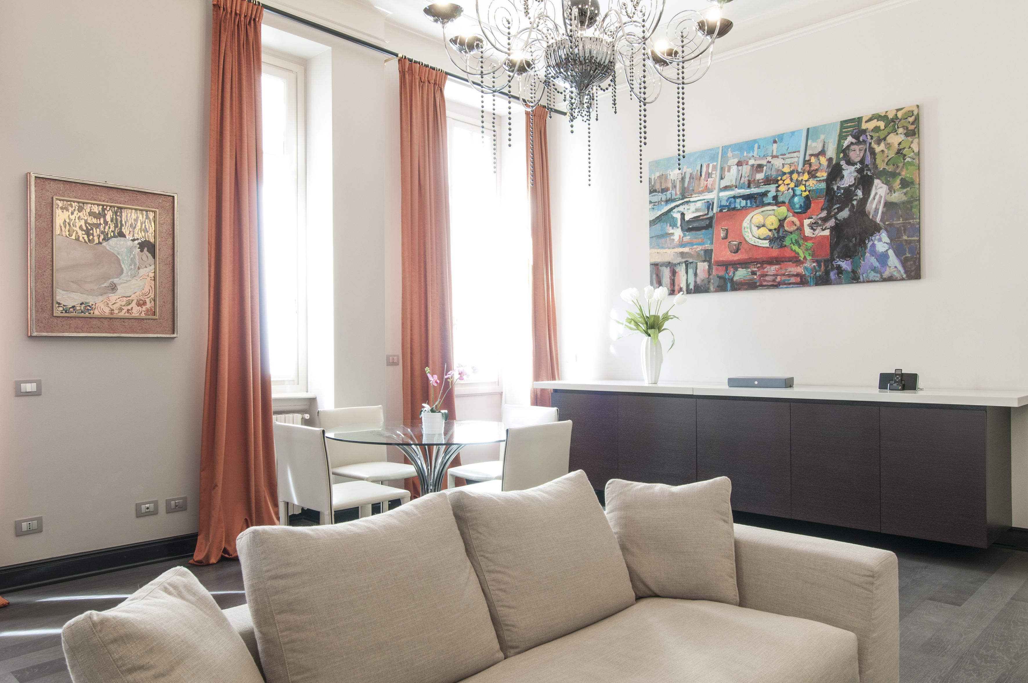 Un salon moderne comprenant un canapé, un coin repas avec des chaises, une table en verre, un coin cuisine avec un comptoir et un lustre.