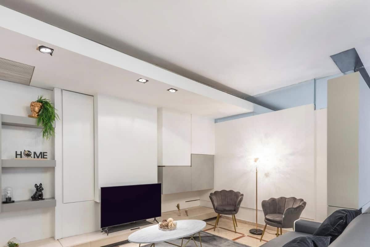 A modern living room with a flat-screen TV, a coffee table, and two armchairs.