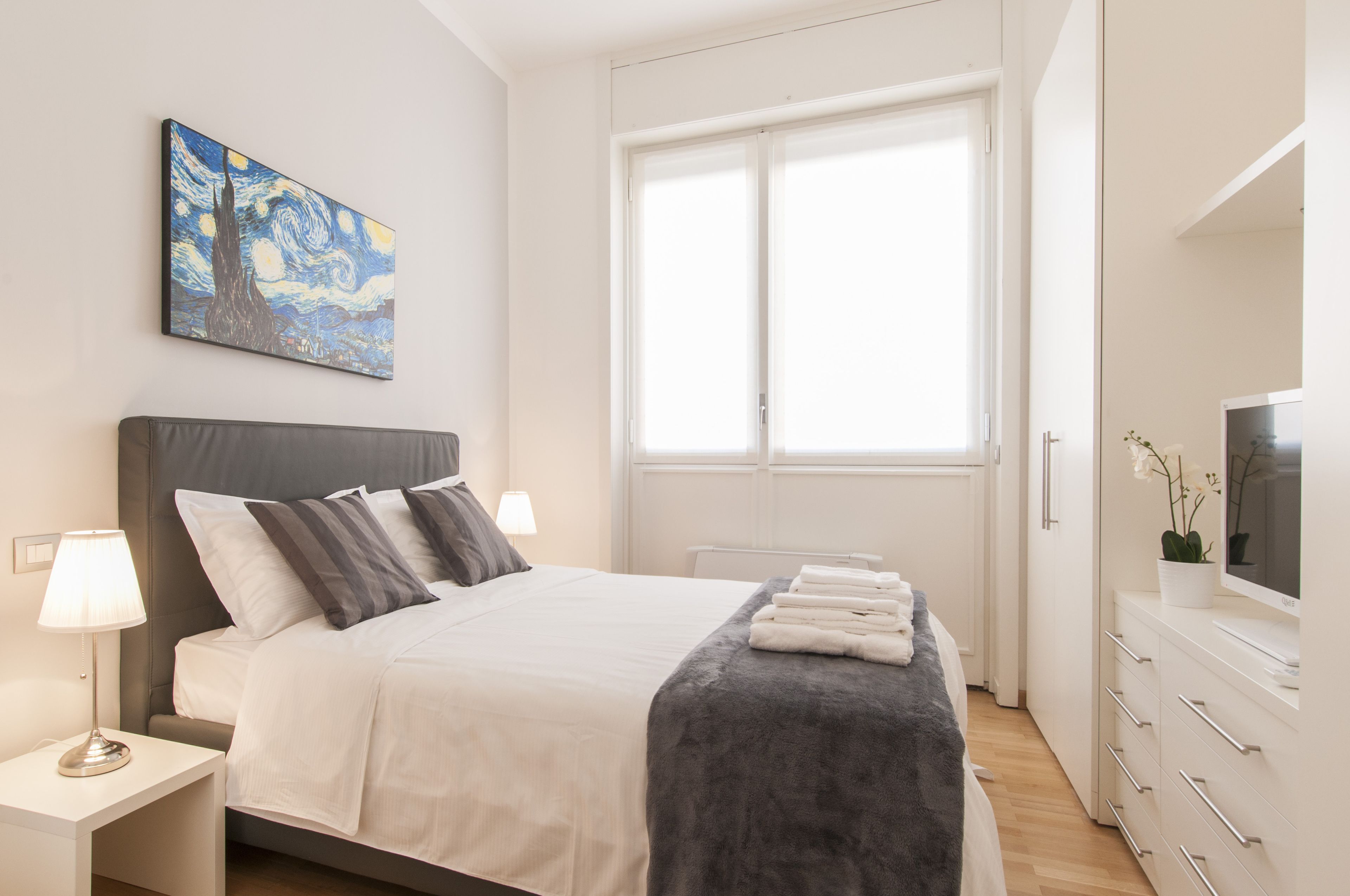 A modern bedroom with a bed, bedside tables, a TV, and a large window.