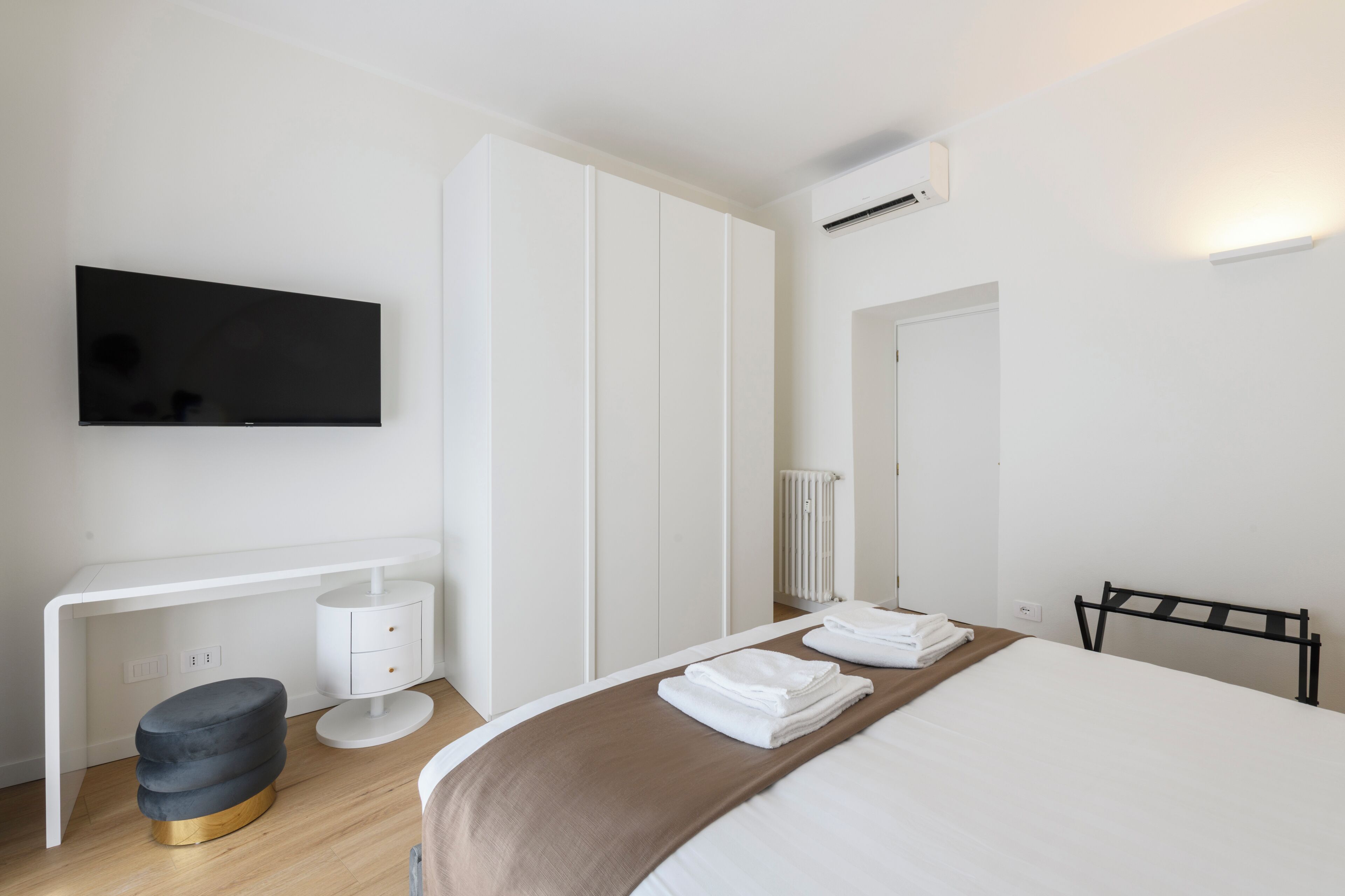 A modern hotel room with a bed, a desk, a chair, a TV, and a radiator.