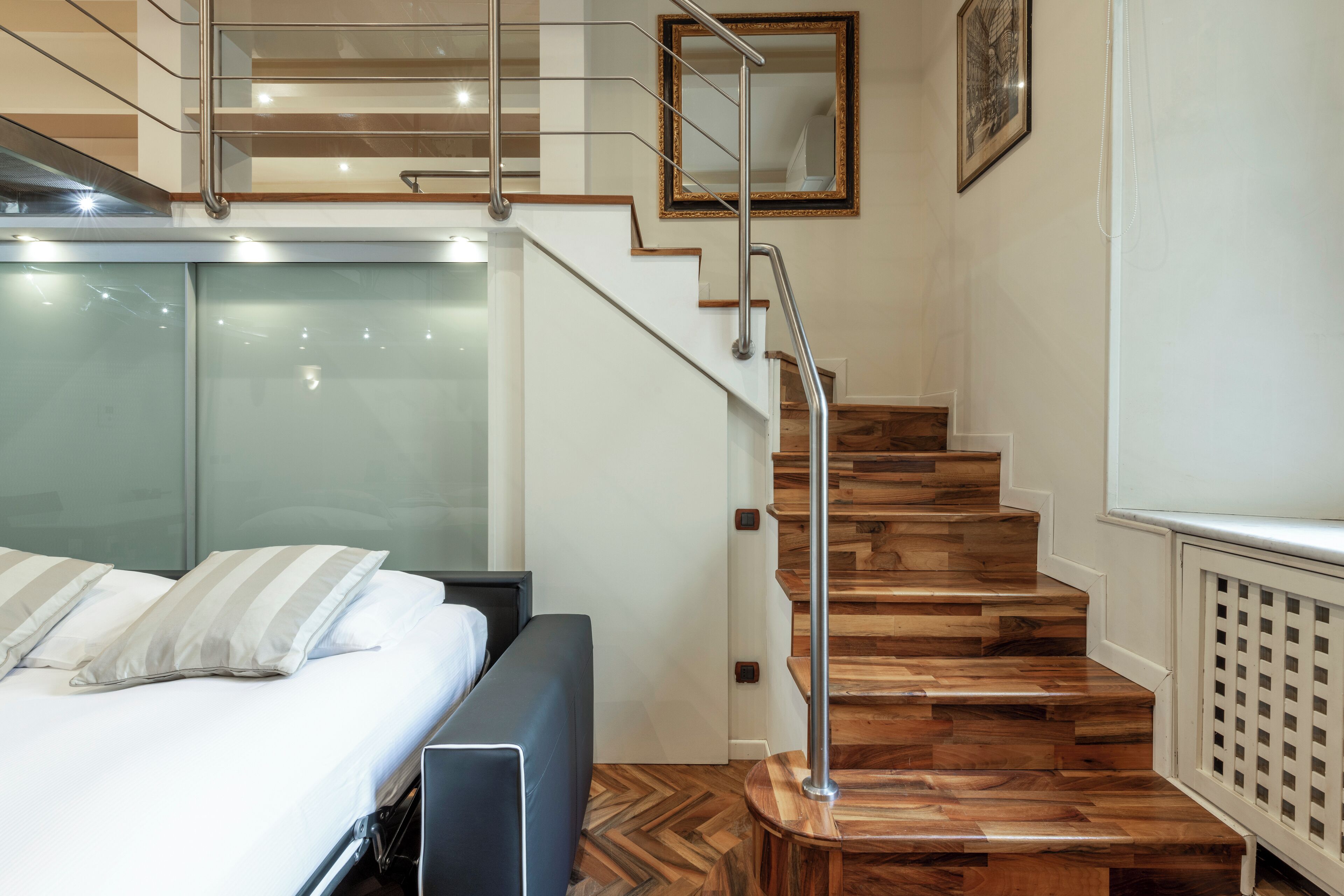 Une chambre d’hôtel moderne avec un escalier en bois, un lit avec une literie blanche et un grand miroir au mur.