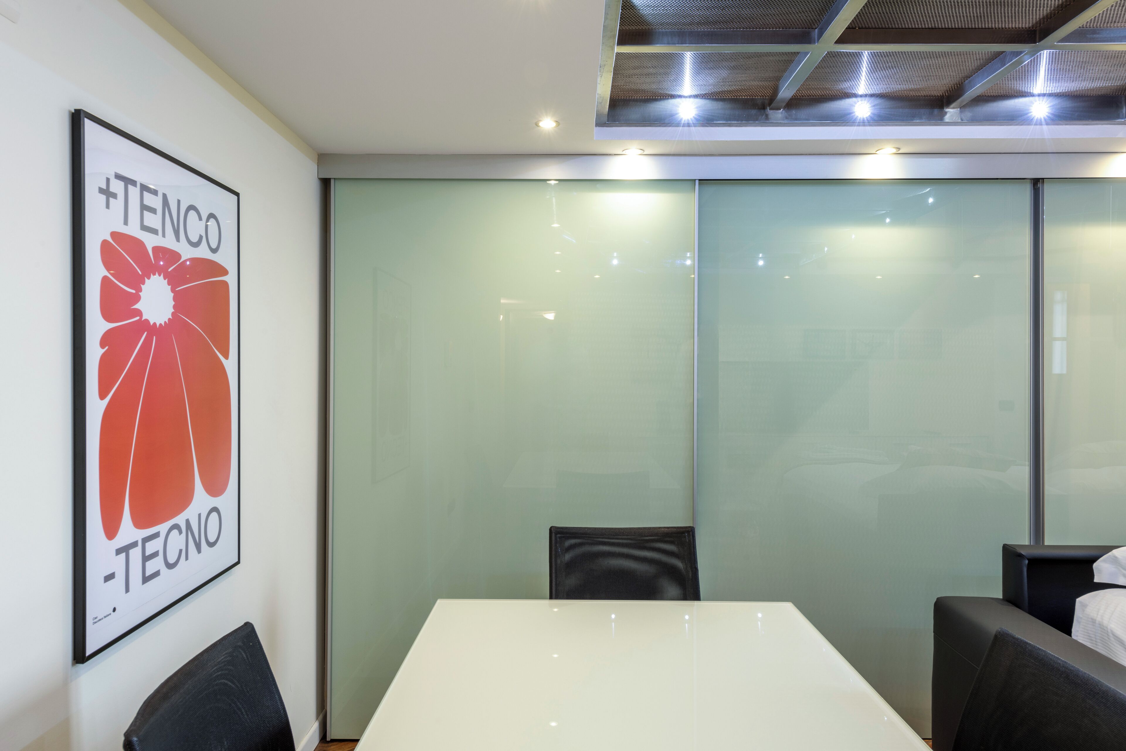 A conference room with a white table, black chairs, a glass partition, and a framed sign on the wall.