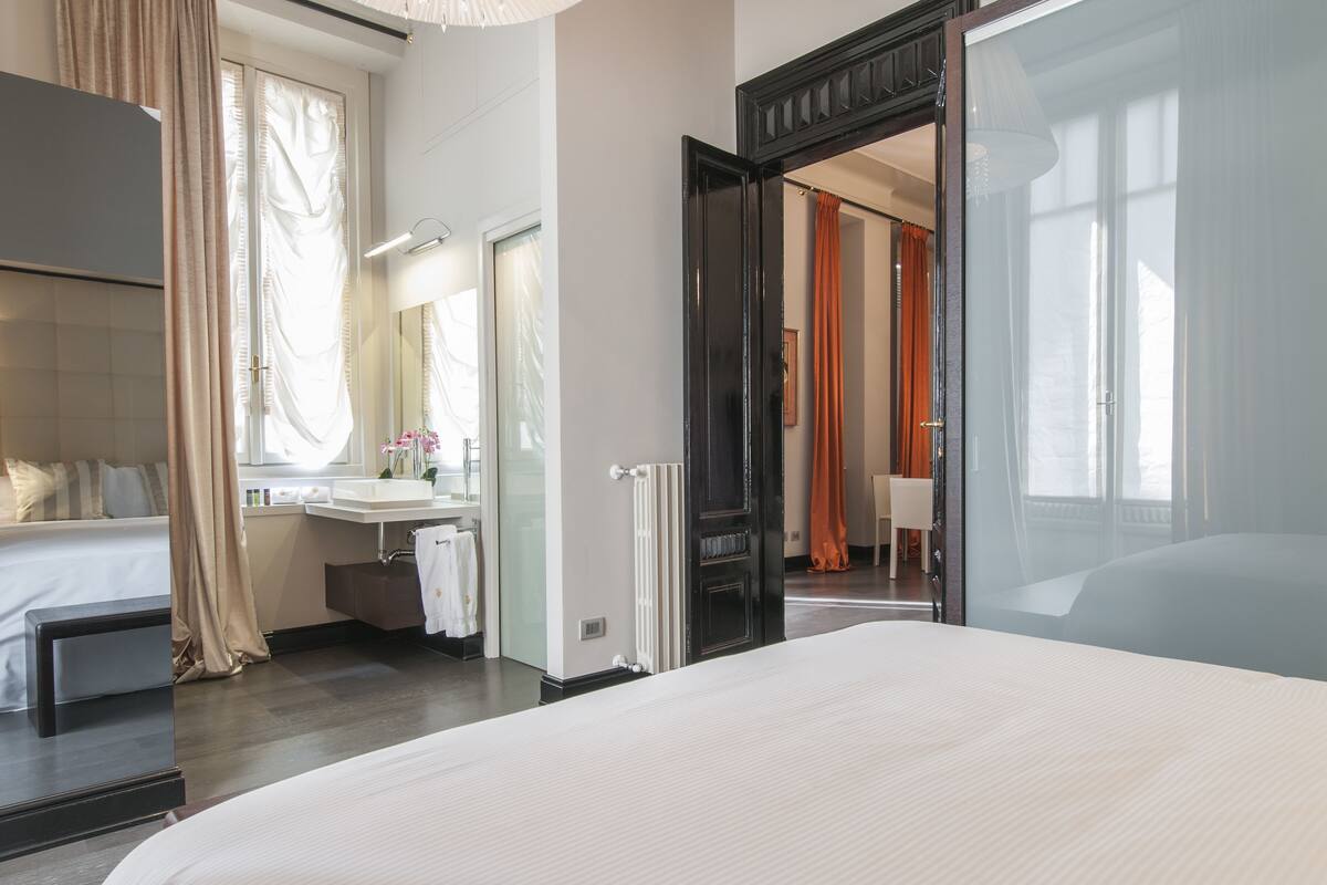 A modern hotel room with a large bed, a bathroom with a sink and mirror, and a view of the outside.