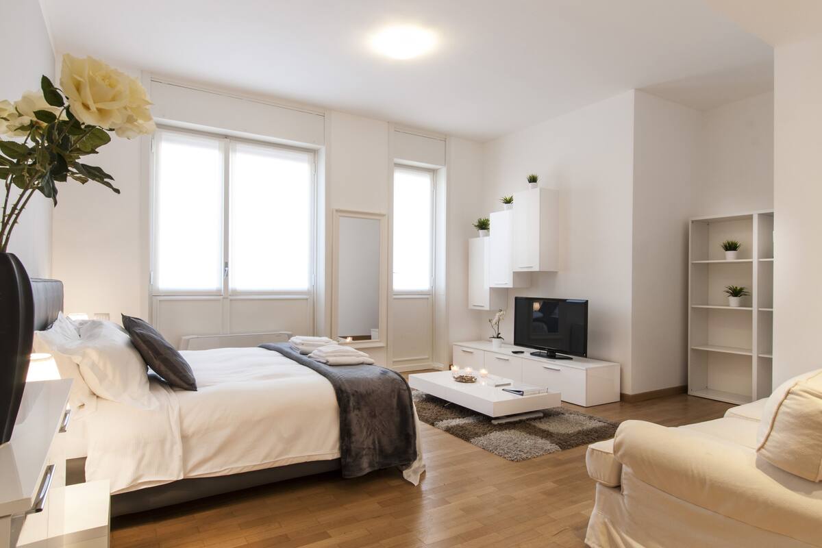 A modern bedroom with a bed, bedside table, and a TV on a white cabinet.