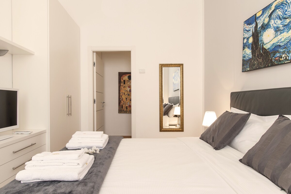 Ein Hotelzimmer mit Bett, Fernseher, Spiegel und einem Gemälde an der Wand.