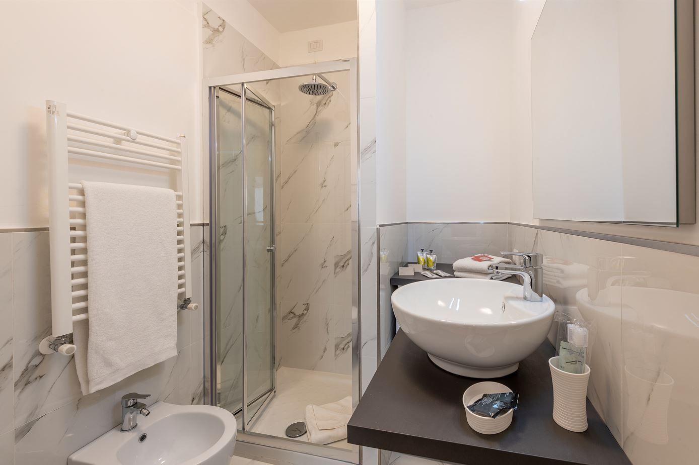 Une salle de bain moderne avec une douche en verre, un lavabo blanc et un meuble-lavabo avec des articles de toilette.