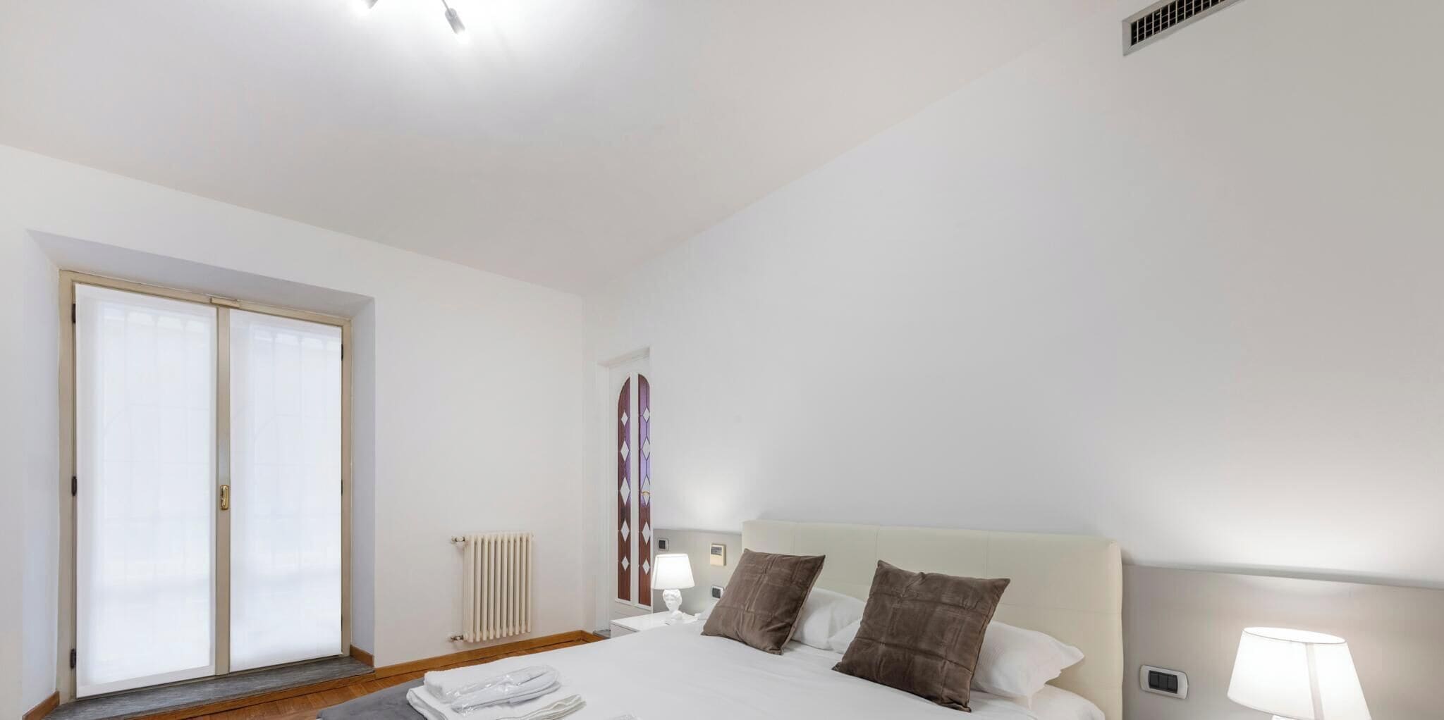Une chambre avec un grand lit, un radiateur, une fenêtre avec des stores et une porte.